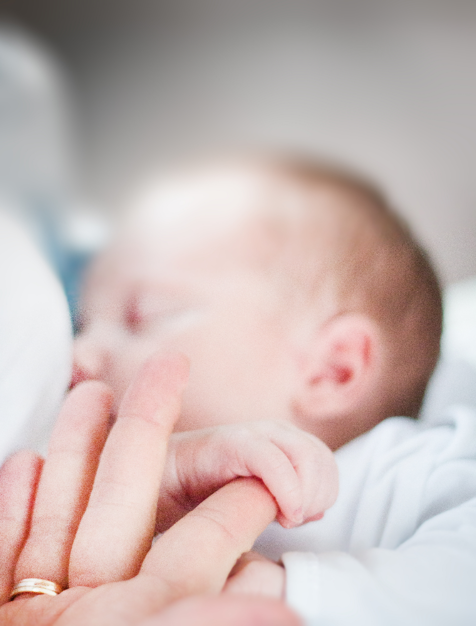 A newborn holding a parent's finger while sleeping